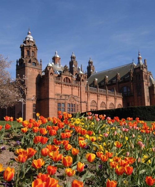 Glasgow's Kelvingrove Art Gallery and Museum on a spring day. There are red and yellow tulips in the foreground, as well as a tree with no leaves.