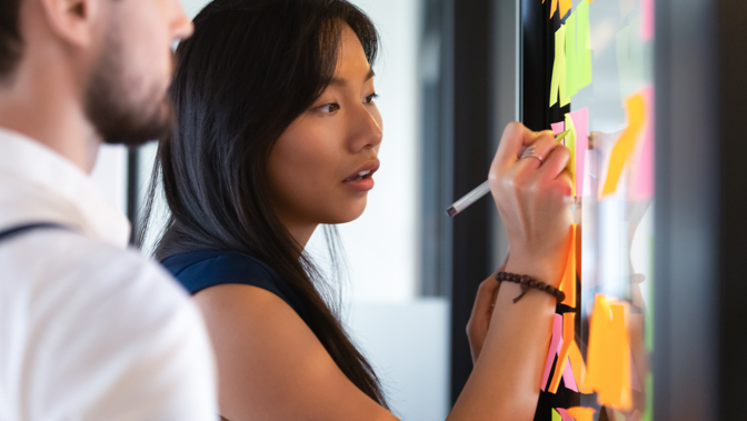 Two people writing on post it notes on a board