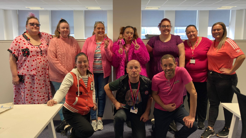 A group of ten people wearing pink and posing for a photo in an open-plan office