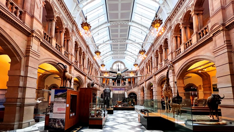 A view of Kelvingrove Museum's west court. A Spitfire aircraft hangs above object displays.