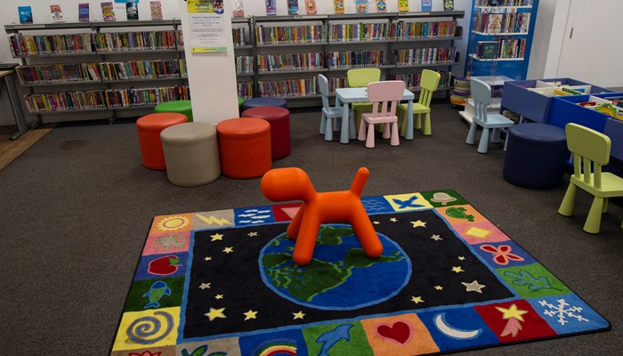 Spacious and colourful children's area at Anniesland Library. There are tables and chairs in the middle of the area, a rug and colourful soft stools.