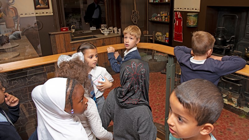 Photograph shows a group of children on a school visit to the People’s Palace looking at the 'single end' display showing life in a tenement flat.