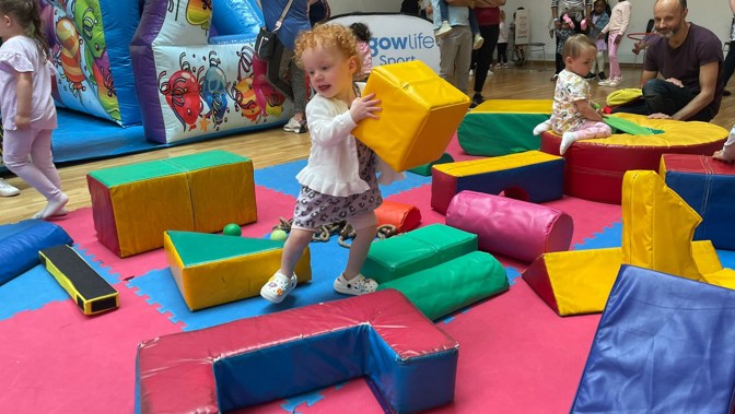 A young child in a soft play area holding a yellow soft play cube