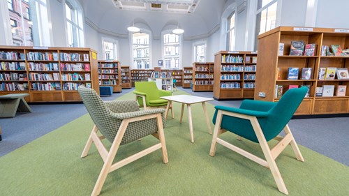 Three colourful chairs are sat around a small wooden table in Partick, with rows of full bookcases visible in the background.