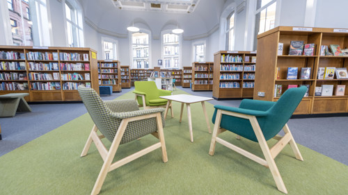 Three colourful chairs are sat around a small wooden table in Partick, with rows of full bookcases visible in the background.