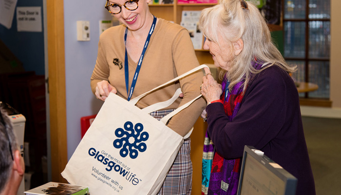 Two volunteers in a library putting books in a canvas bag