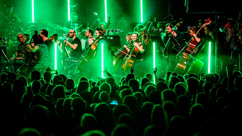 Orchestral musicians on stage at Barrowland Ballroom in front of crowd with green lights filling the room