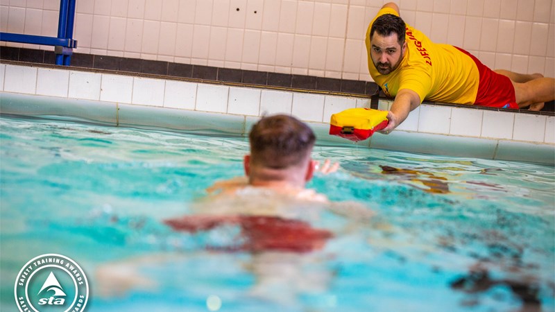 Lifeguard reaching out a float to a person in a swimming pool