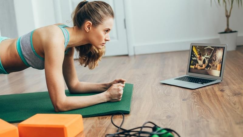 female in her home doing the plank while watching an exercise class on her laptop in front of her