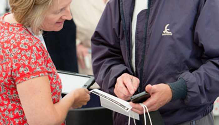 An adult asking Family History staff questions and showing something on their phone, holding a Family History bag.