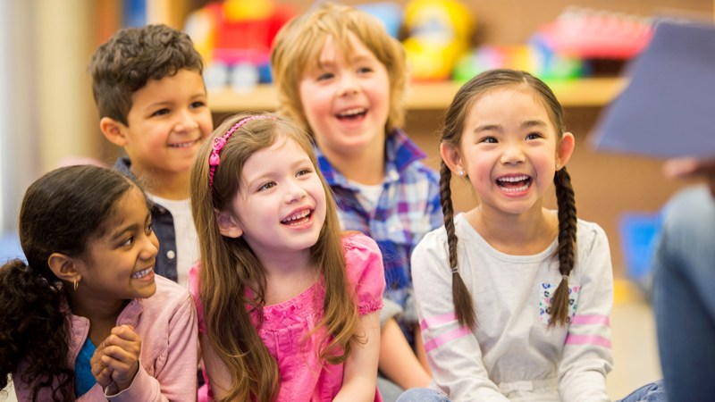 South, East Asian and white kids sitting together in a library and smiling.