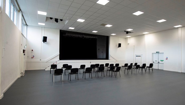 large meeting room with several black chairs facing the front of the room where there is a large black screen and speakers