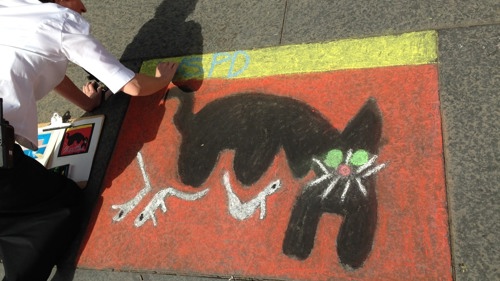 Photograph of a child drawing shapes onto a school playground using chalk