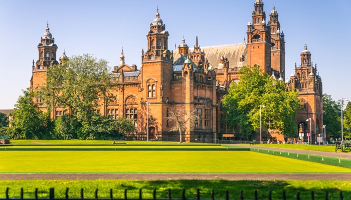 exterior shot of a red sandstone museum which is grand and has pillars at the front. the museum is surrounded by green trees and grass