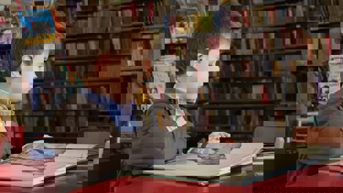 A child sits at a library desk, looking through a picture book