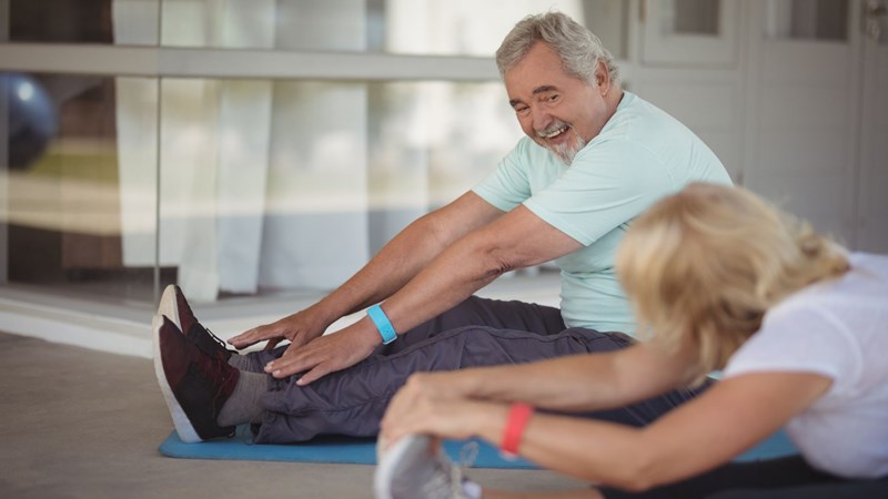 image of a man and women sitting on floor in a gym stretching out to touch their toes