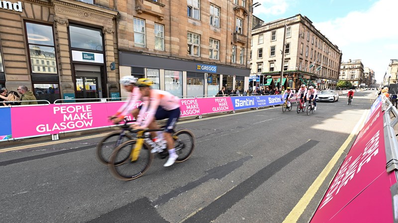 Cyclists in George Square during the UCI World Cycling Championships passing roadside board with the People Make Glasgow branding.