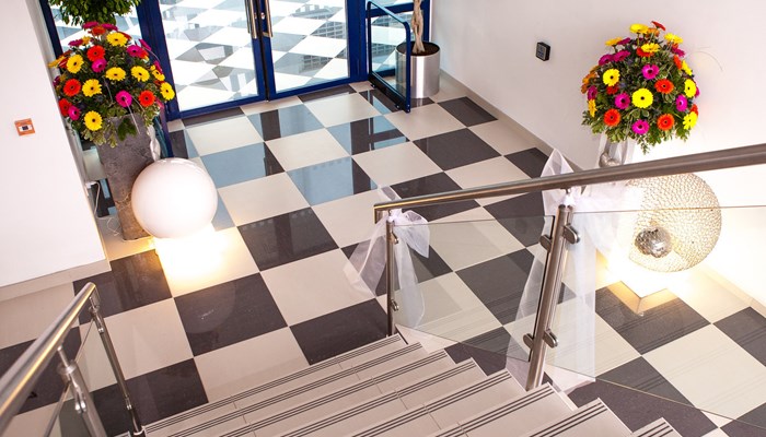 staircase with black and white checked flooring at the bottom. there are white ribbons attached to the the banister ready for a wedding. There are also two flowers arrangements at the door just beyond the bottom of the stairs