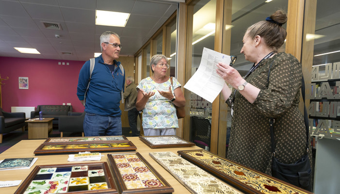 Visitors view decorative tile samples as a member of staff leads a museum outreach session.