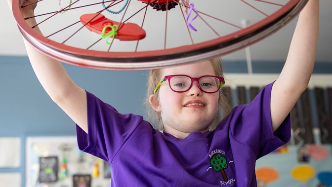 A school pupil shows off an artwork made from a bicycle wheel