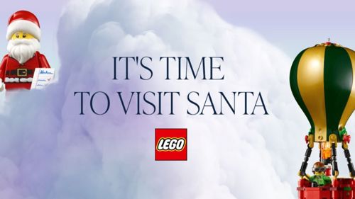 LEGO-themed holiday advertisement featuring a LEGO Santa figure holding a letter on the left and a green-and-gold LEGO hot air balloon with a minifigure inside on the right. In the center, large text reads 'IT'S TIME TO VISIT SANTA' above the LEGO logo, set against a cloudy background