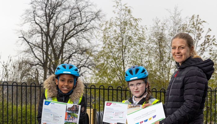 Cyclist holding learning materials standing with two children in school uniform on bikes 
