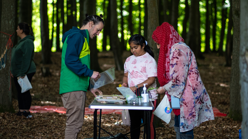 An artist engaged and adult and young teen with books and objects in a wooded area. 