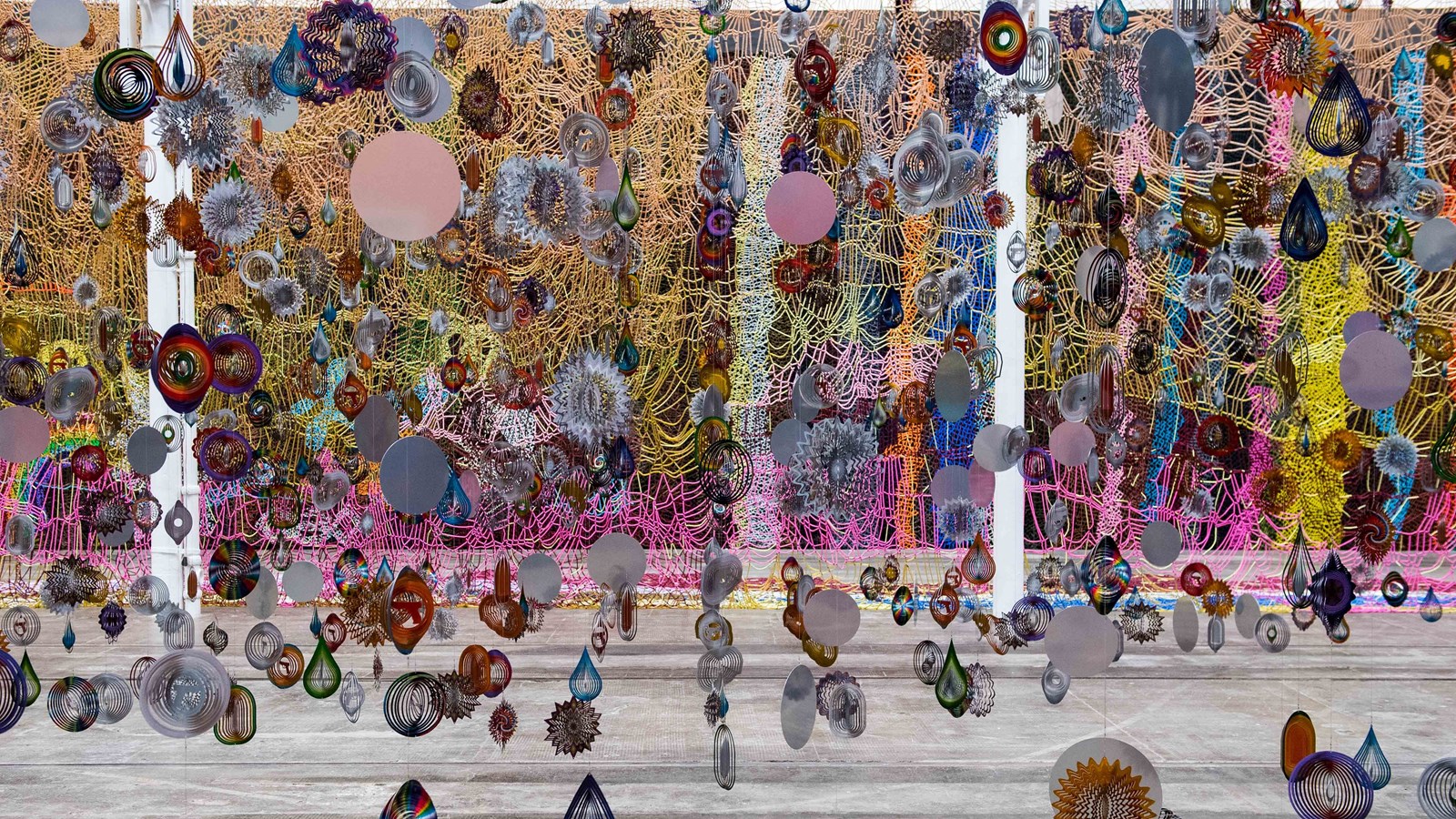 An installation including a multicoloured net and hundreds of baubles hangs in a vast gallery