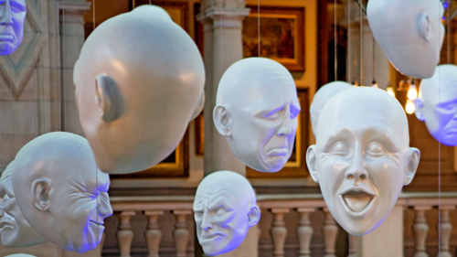 floating head objects suspended from ceiling with different expression in museum gallery setting.