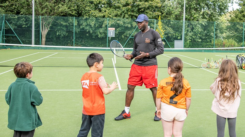 A group of children receiving tennis coaching from coach at Kelvingrove tennis courts. 