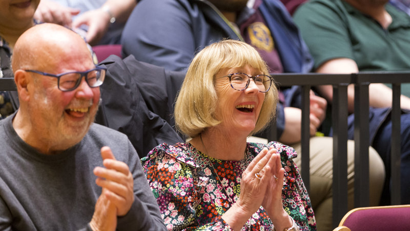 Audience members seated in a theatre applauding during a live event.