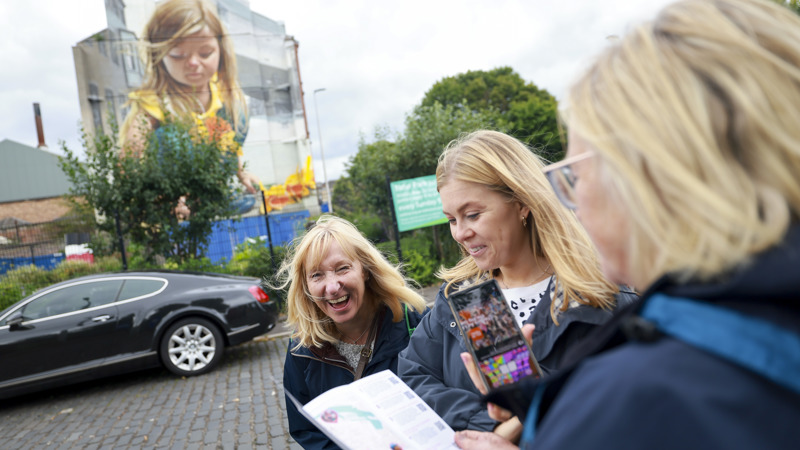 Three visitors pause at one of Govan's murals to hear about its musical links