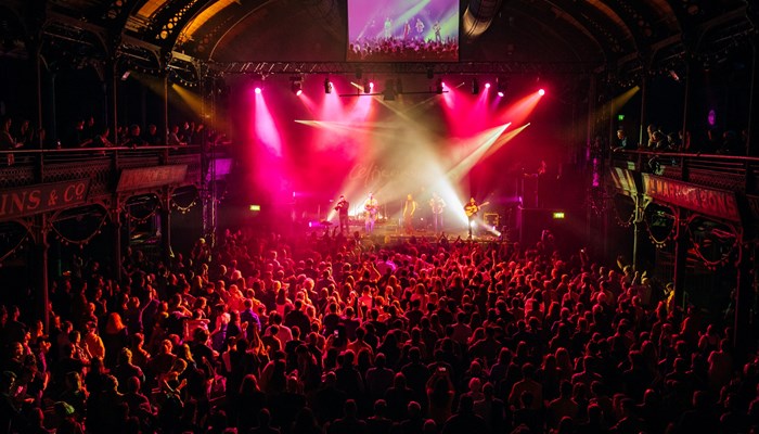 A large concert venue, packed with hundreds of revellers, dramatic light focused on a stage