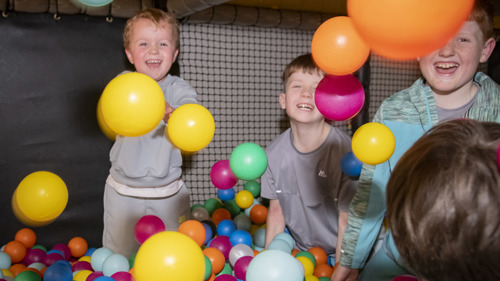 A group of four young people smiling and laughing while playing in a colourful ball pool