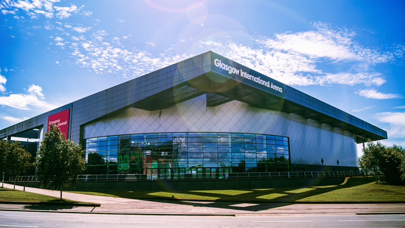 Exterior view of Glasgow's arena building on a sunny day, with the distinctive curved roof and glass frontage.