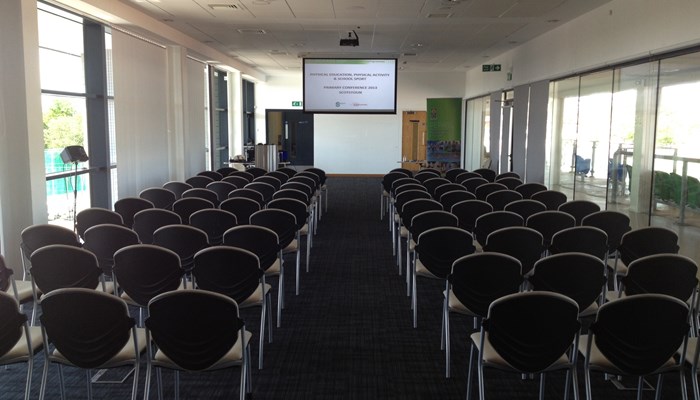 large meeting room with chairs on either side looking forward towards a screen and projector at top of room
