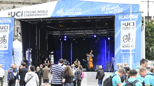 Musicians performing on the main stage in the George Square fan zone during the 2023 UCI Cycling World Championships. Two are sitting playing guitar while one is standing playing double bass and another the keyboard.