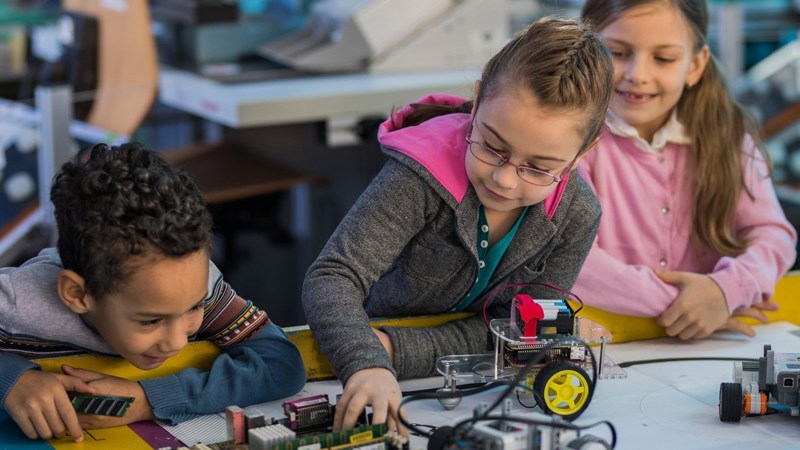 Three children smiling and playing with Lego models as part of a science and technology club.