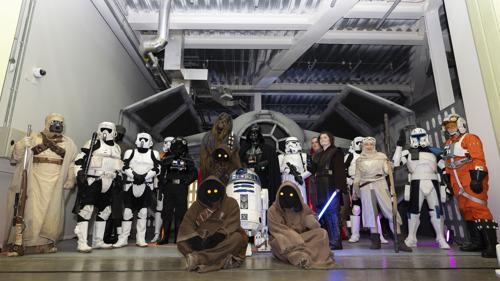 Characters from a science fiction space saga stand in front of a space speeder