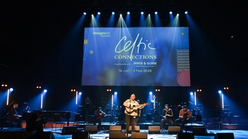 A group of musicians performing on a lit stage. There is a pianist, guitar player and violinist