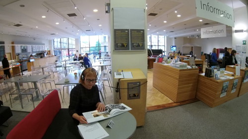 A person sits in The Mitchell Library, listening to an sound work through headphones and viewing exhibition materials.