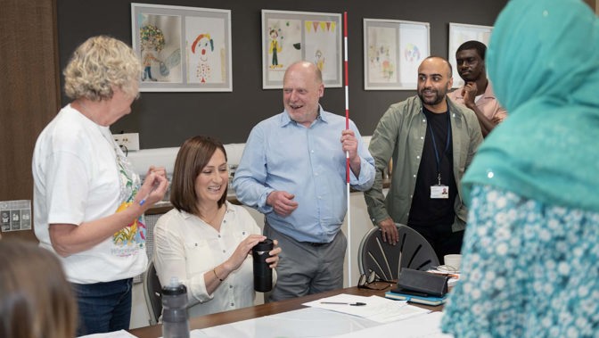 Group gathered round a table during a workshop, with one person holding a white cane and others engaged in discussion.