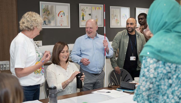 Group gathered round a table during a workshop, with one person holding a white cane and others engaged in discussion.