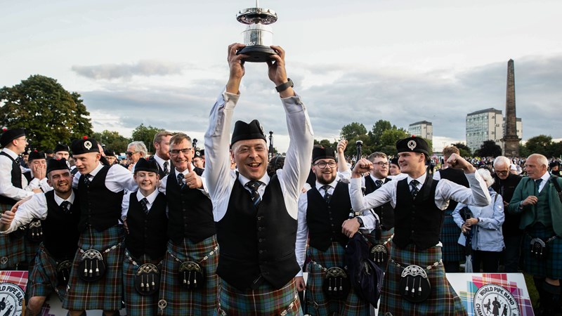 Members of Peoples Ford Boghall & Bathgate Caledonia Pipe Band smiling and holding a trophy after winning the 2023 World Pipe Band Championships.