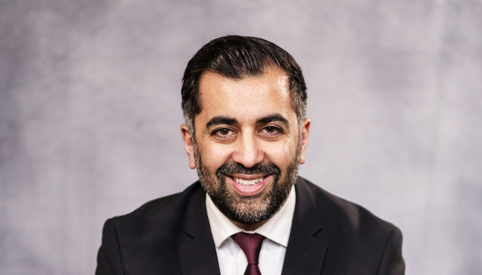 A mean wearing a dark suit and tie and white shirt is sitting down