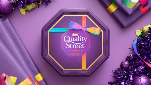 A purple tin wrapped in ribbon which says 'Quality Street' on it against a purple background