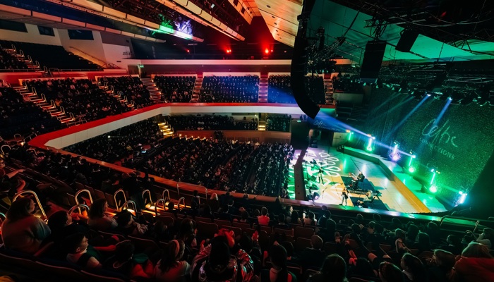 A high-angle view of a packed concert hall audience watching a band perform on a stage with the "Celtic Connections" logo.