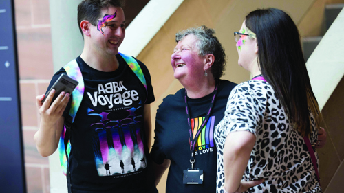 A group of three people laughing together in a museum lobby. They have colourful designs painted on the sides of their faces