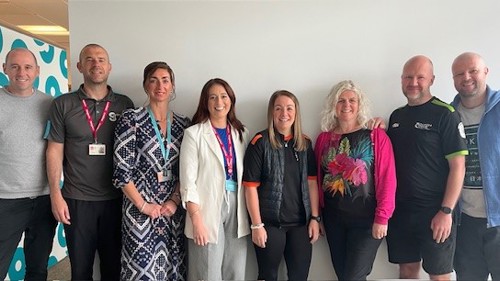 A group of eight people standing together for a group photo in an office meeting room