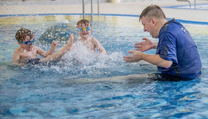 Two children laughing and splashing a swimming coach while in the pool